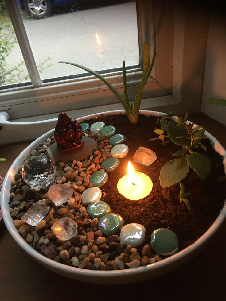 a bowl filled with rocks and candles on top of a table next to a window