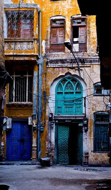 an old building with blue and green doors in the middle of it's alleyway