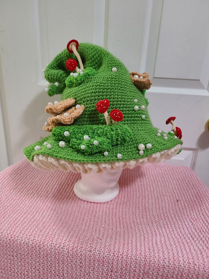 a knitted green hat with mushrooms on it sitting on top of a white table