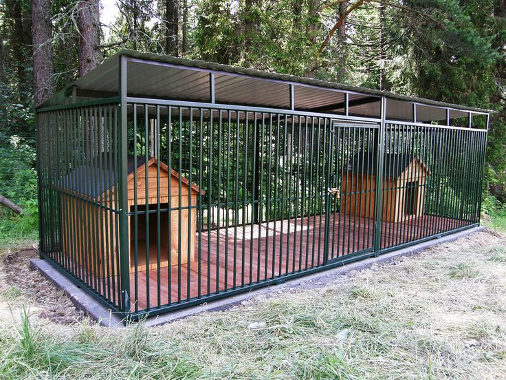 a dog house is in the middle of a fenced in area with grass and trees