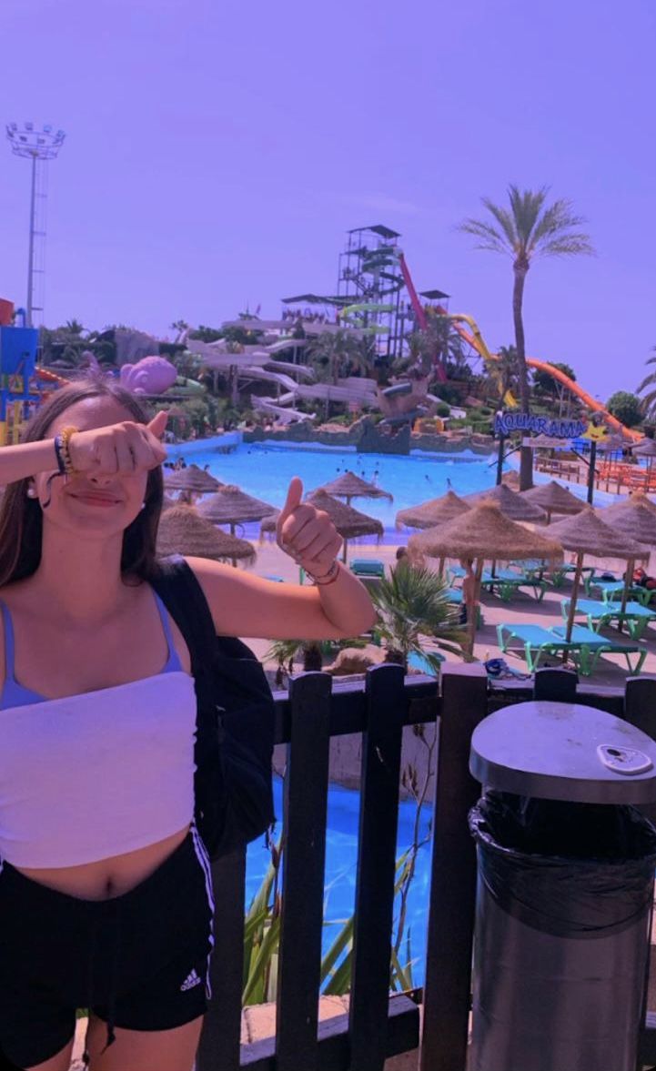 a woman standing on top of a wooden fence next to a swimming pool with water slides in the background