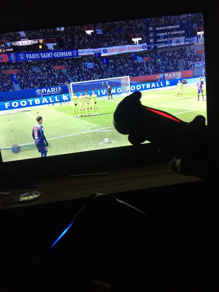 a person holding a remote control in front of a tv with a soccer game on it