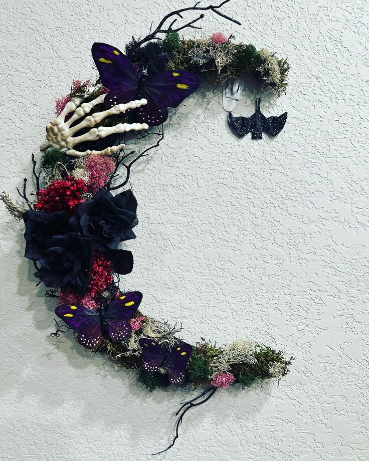 a wreath made out of branches and flowers with two butterflies on the wall behind it