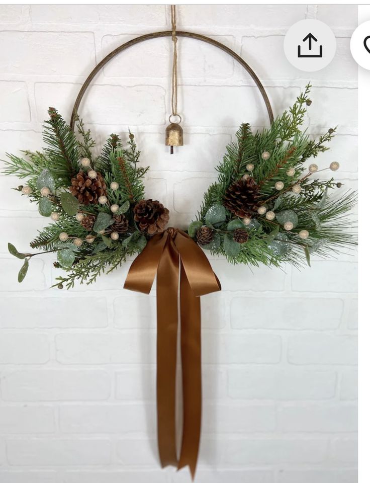 a christmas wreath with pine cones and greenery hanging on a brick wall next to a gold ribbon