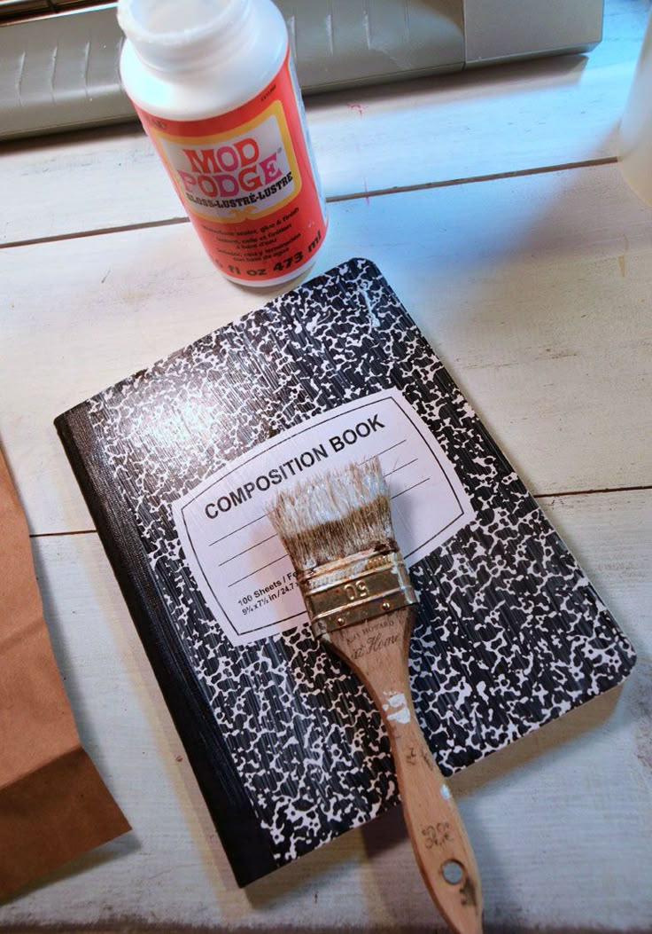 a paintbrush sitting on top of a book next to a glue bottle and paper bag