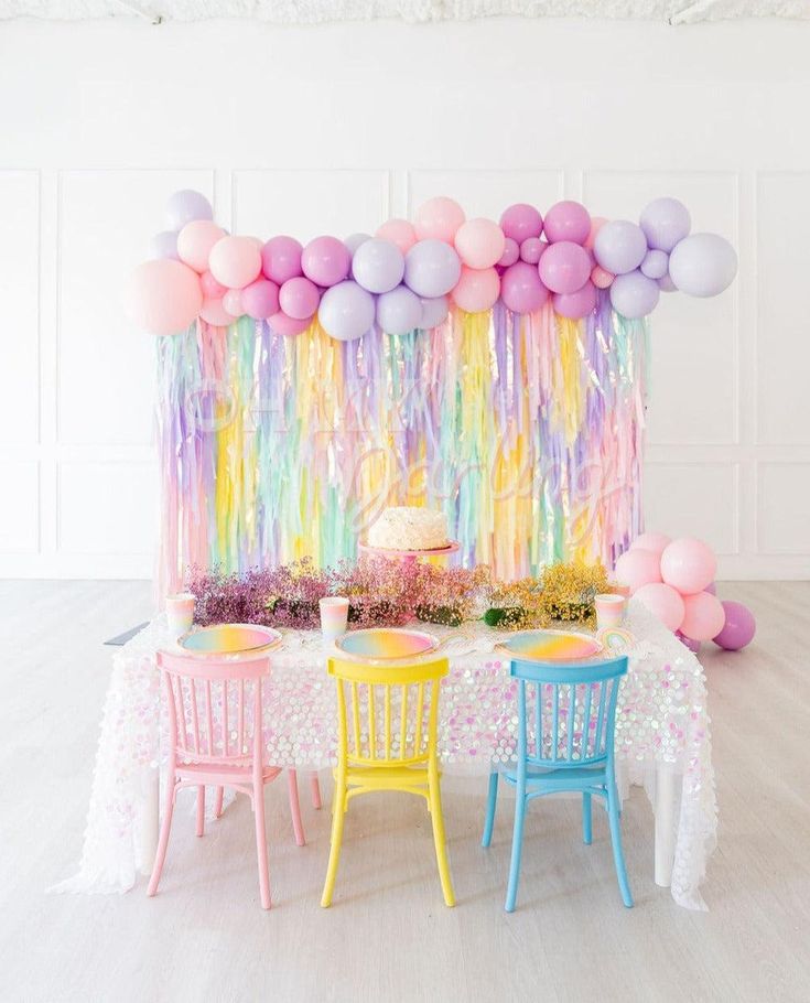 a table topped with balloons and cake next to two chairs in front of a white wall