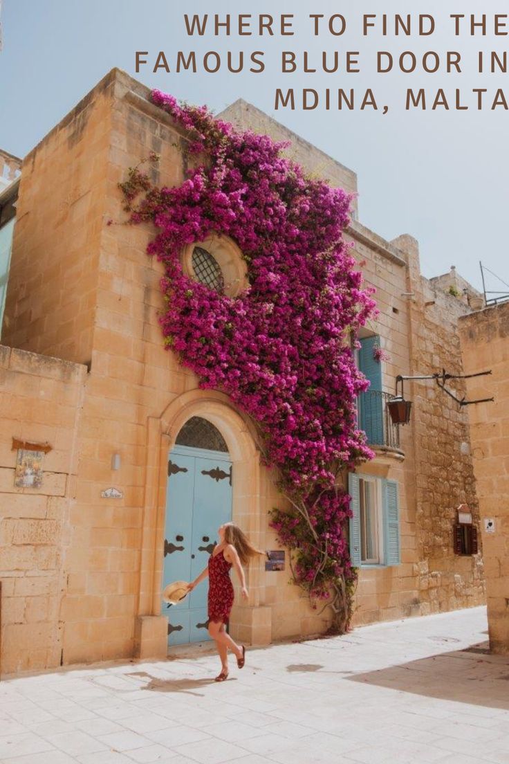 a woman in a red dress walking past a building with purple flowers on the side