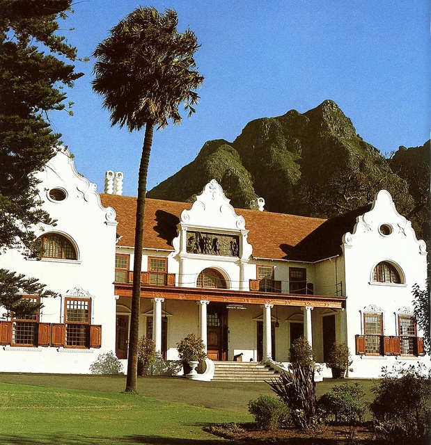 a large white house with red shutters and palm trees in front of it on a sunny day