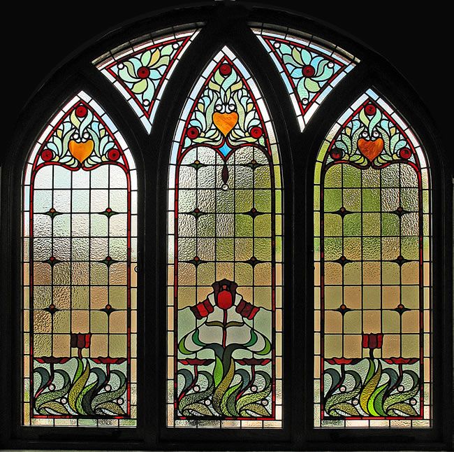 a large stained glass window with flowers and leaves on it's sides, in a dark room