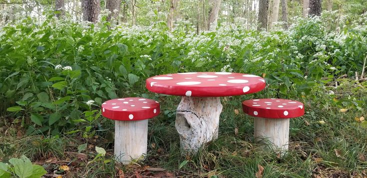 three red and white mushrooms sitting on top of a tree stump in the grass next to bushes