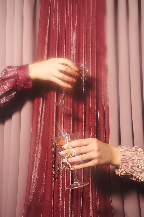 a woman's hand holding a wine glass in front of a curtain with red drapes