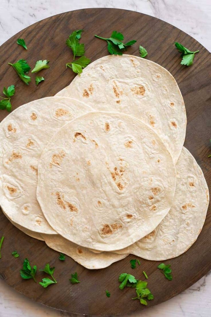 three tortillas on a wooden plate with parsley sprigs around them