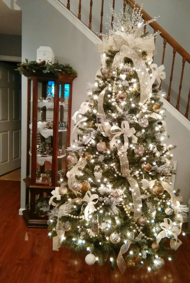 a decorated christmas tree with white and silver ribbons on it in front of a banister