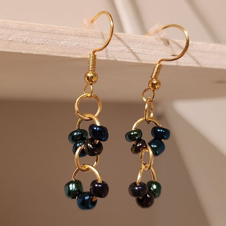 a pair of gold - plated earrings with black and green beads hanging from them