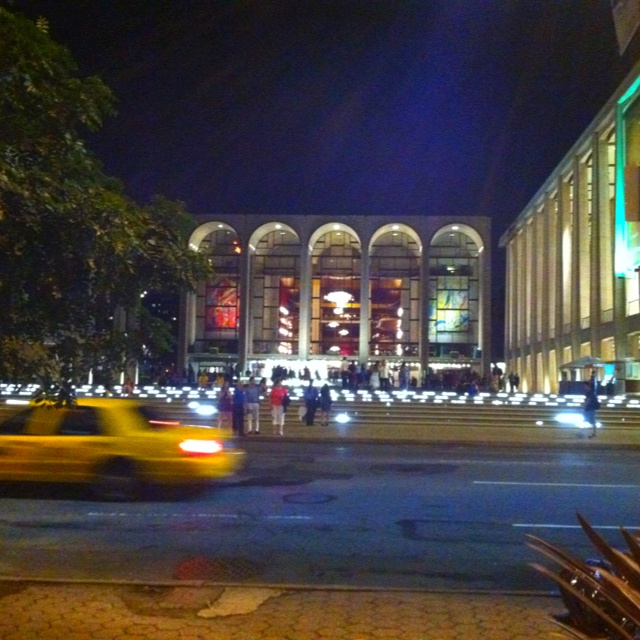 a yellow taxi driving down a street next to tall buildings with arches on the sides