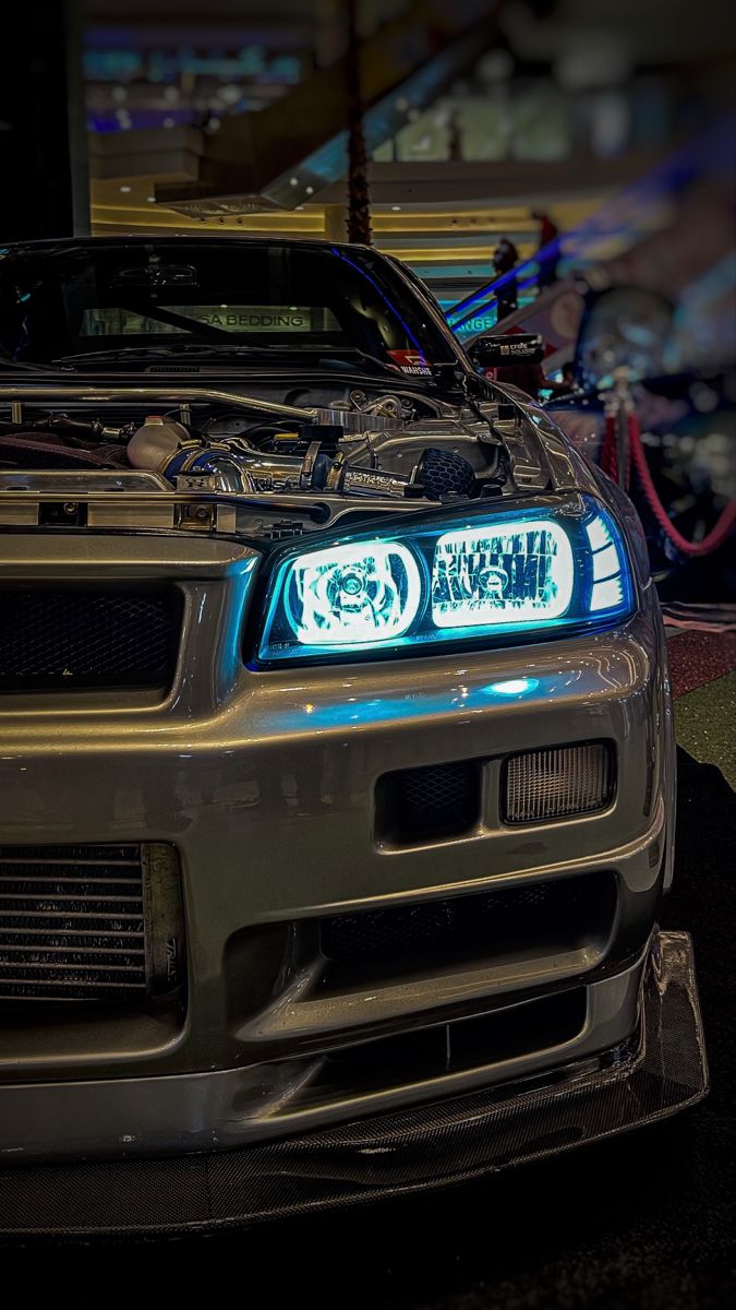 the front end of a silver car with its hood up and lights on at night