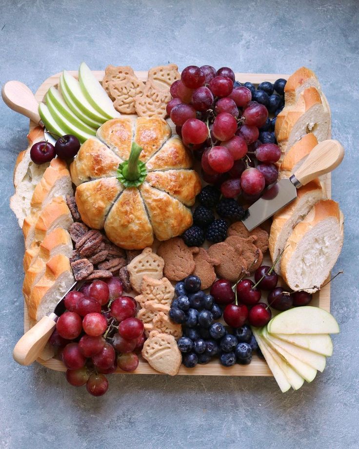 a platter filled with bread, grapes, apples, and other food on top of a table