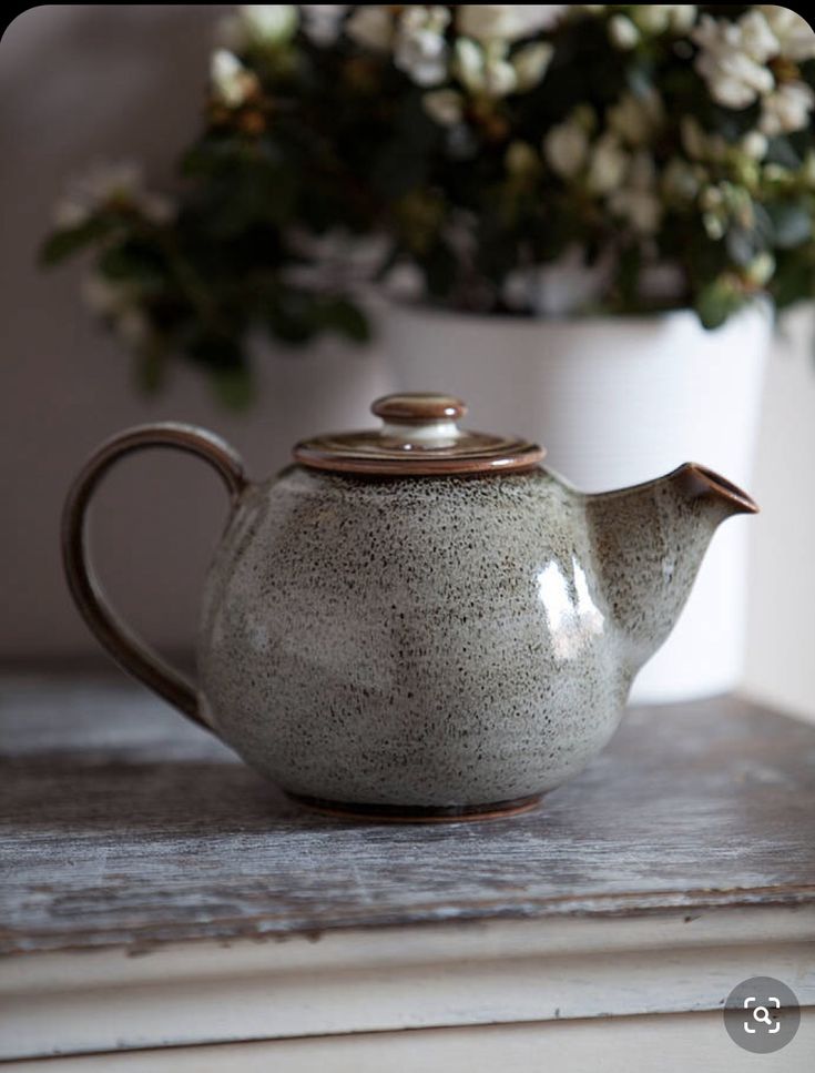 a ceramic tea pot with a wooden lid on a table next to a flower arrangement