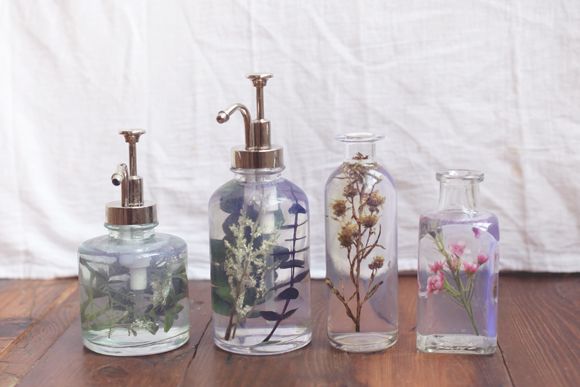 four glass bottles with flowers in them on a wooden table