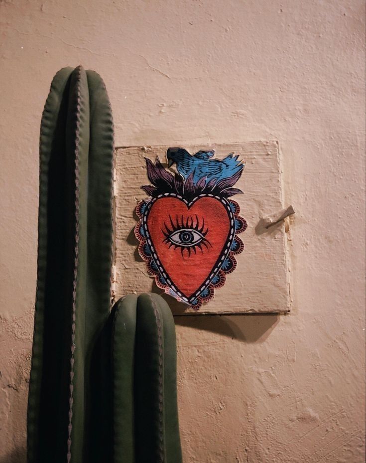 a heart with an eye painted on the side of a wall next to a cactus