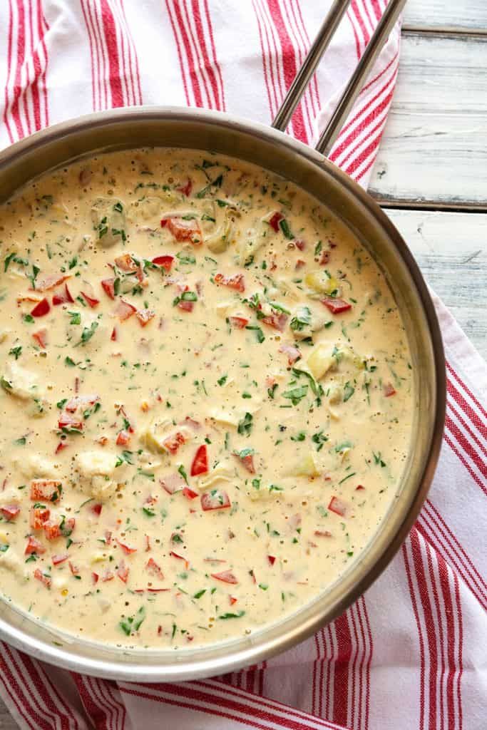 a pan filled with cheese sauce on top of a red and white striped towel next to a spoon