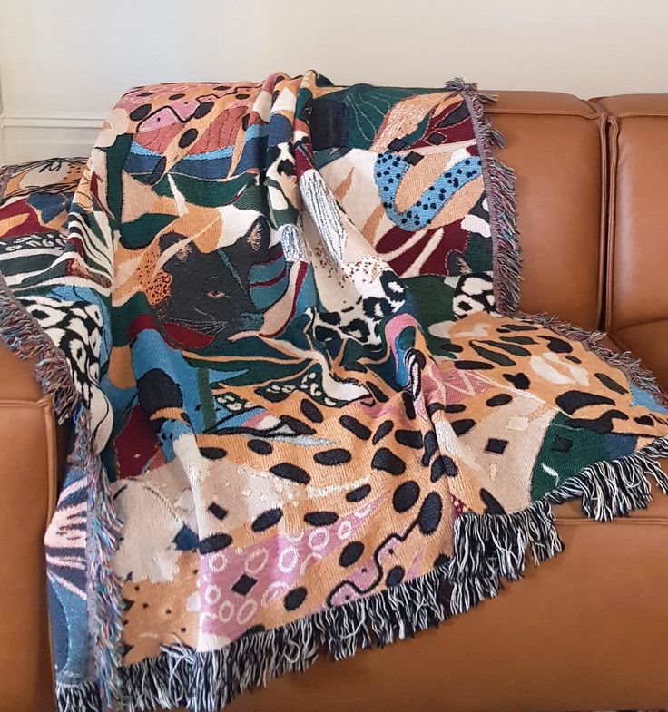 a couch with a blanket on top of it next to a brown leather chair in front of a white wall