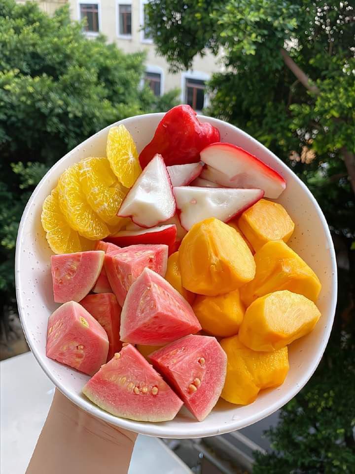 a white bowl filled with cut up fruit on top of a table next to trees