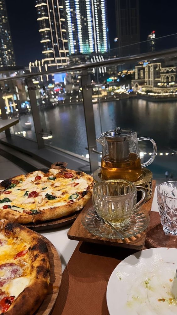 two pizzas are sitting on the table with drinks and water in front of them