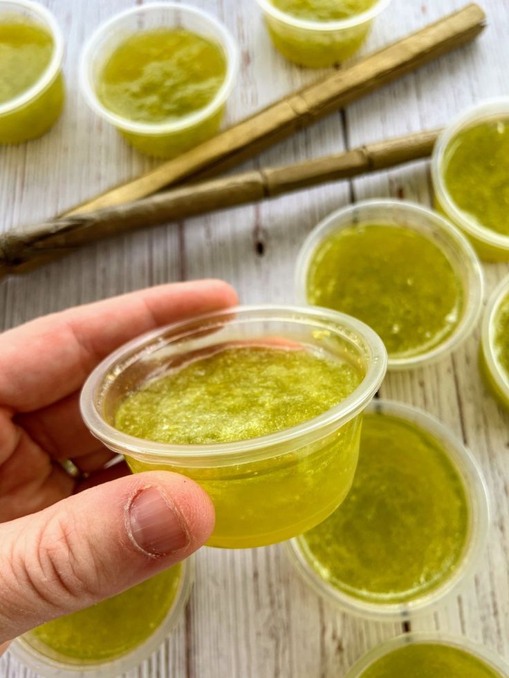 a hand holding a small cup filled with green liquid next to other cups and spoons