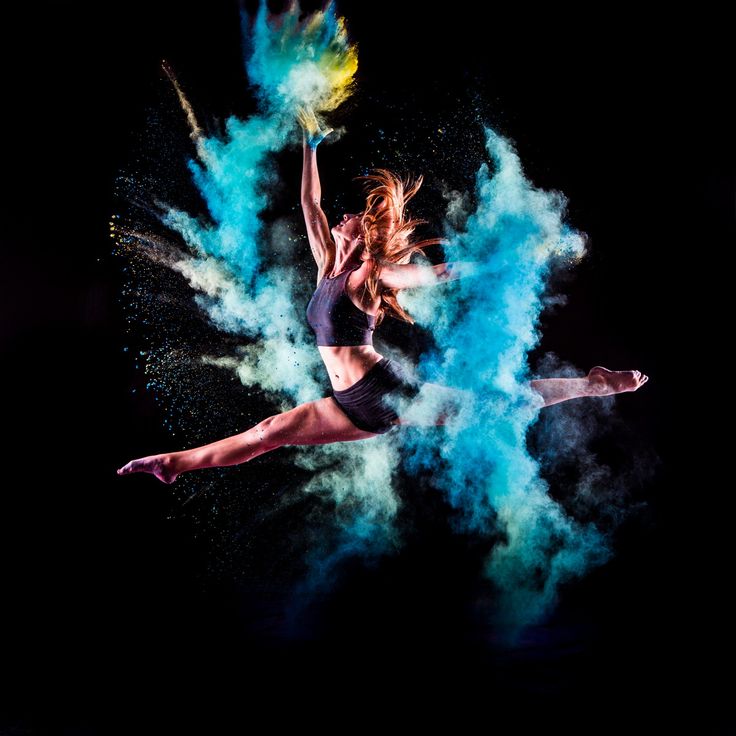 a woman is dancing in the air with colored powder on her body and arms behind her back