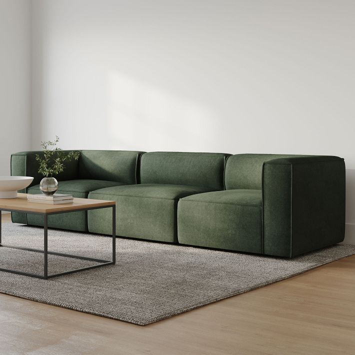 a green couch sitting on top of a wooden floor next to a table and chair