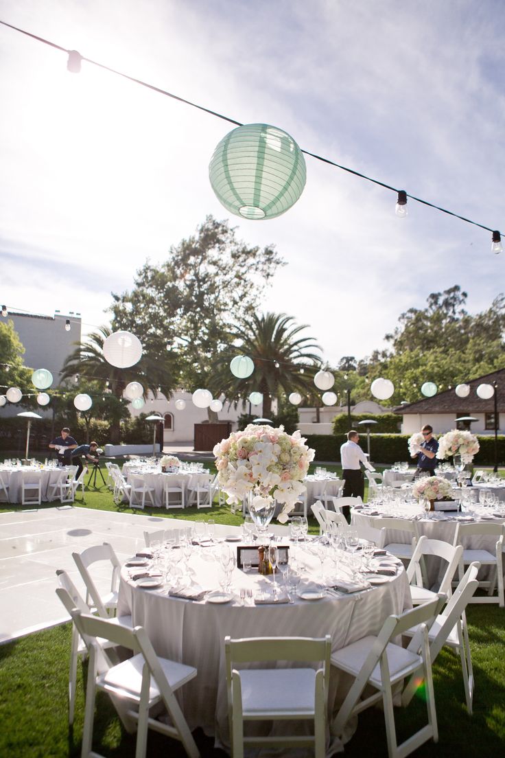 the tables are set up for an outdoor wedding reception with paper lanterns strung from the ceiling