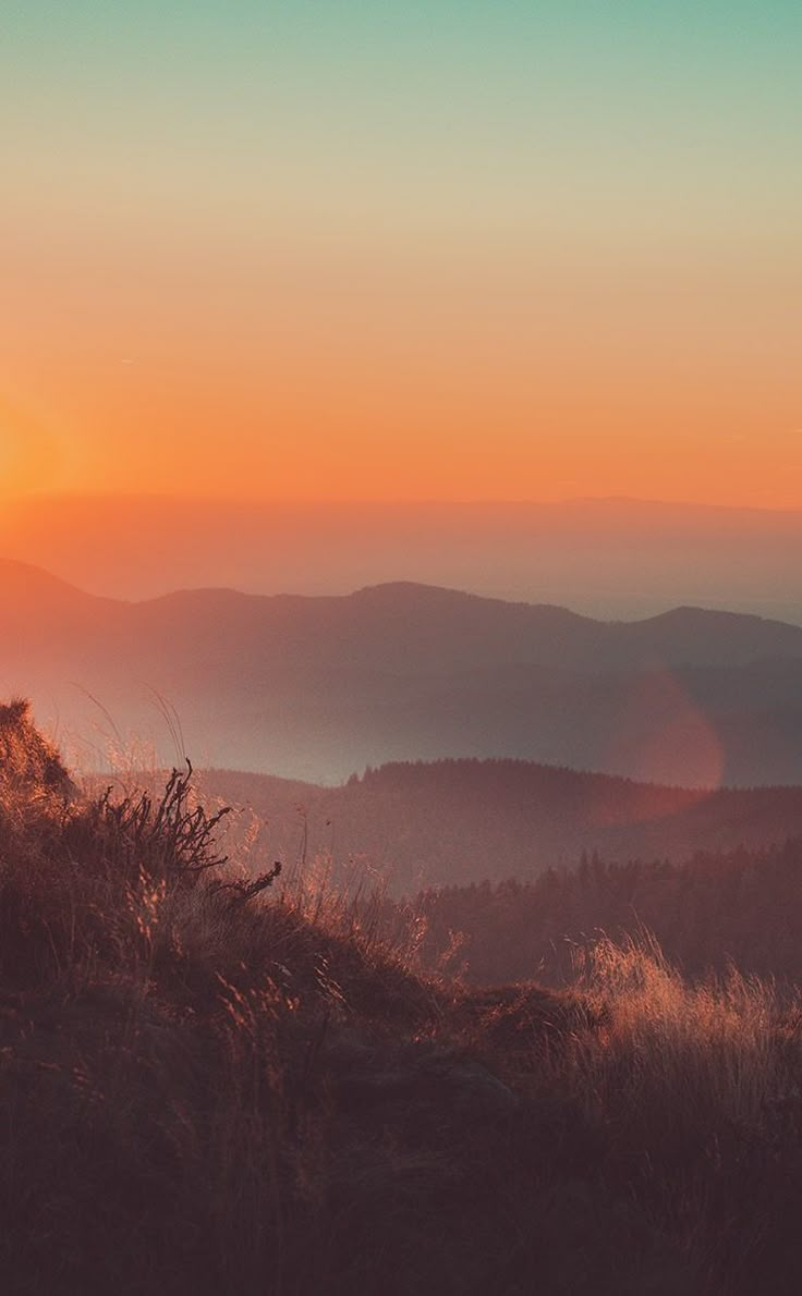 the sun is setting over some hills and trees