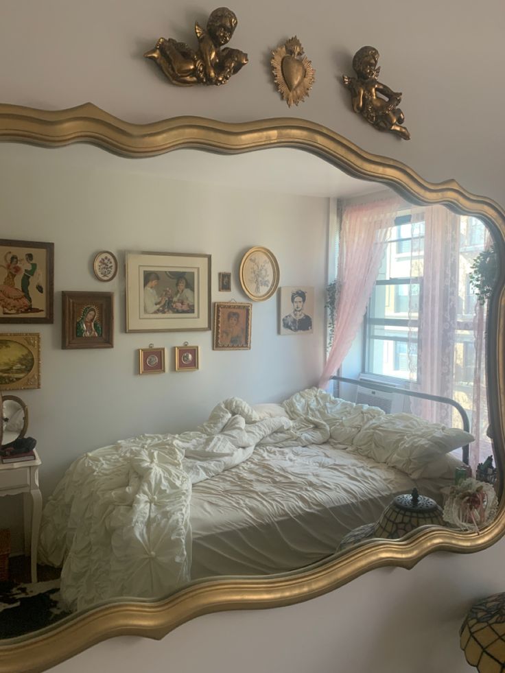 a large mirror reflecting a bed in a room with pictures on the wall above it