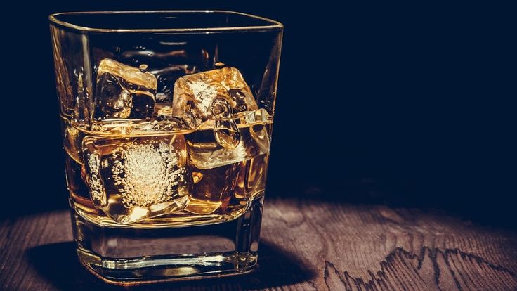 a glass filled with ice sitting on top of a wooden table in front of a dark background