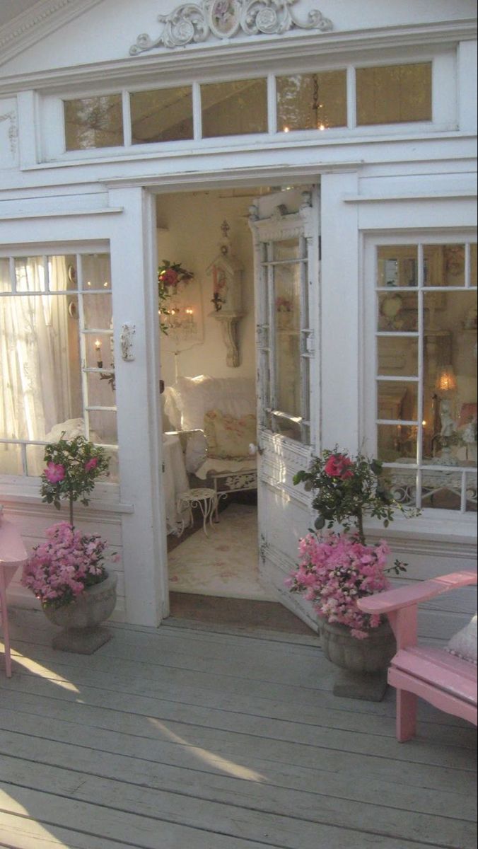 a pink bench sitting in front of a white building with flowers on the porch and windows