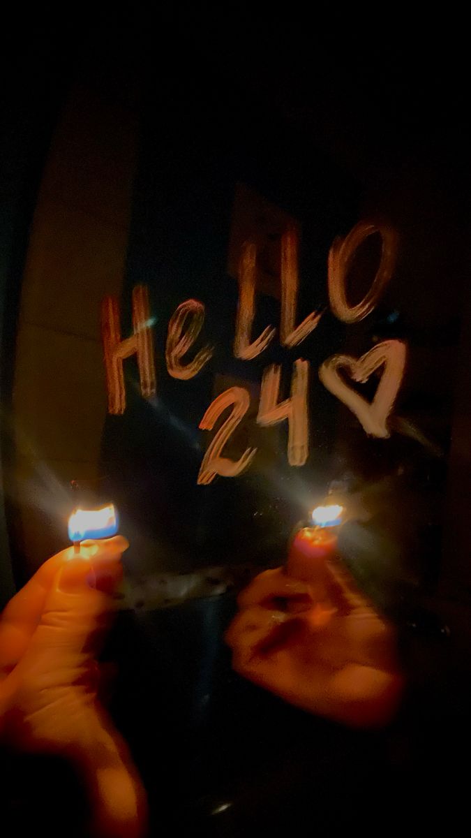 two hands holding small lit candles in front of a sign that says hello 24h2