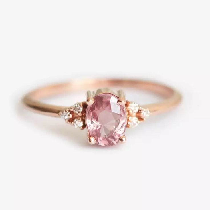 a pink diamond ring with three diamonds on the band and an oval shaped stone in the middle