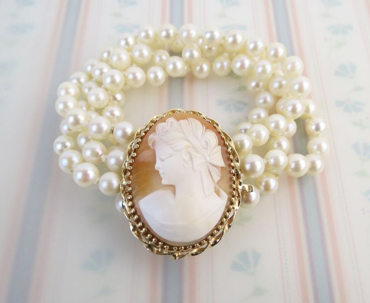 "This Vintage Victorian revival 14k gold pearl bracelet has a wonderful carved shell cameo. The cameo carving depicts a young lady facing left with an elaborate bow in her hair and draped clothing. It is set in 14 karat gold (tested) with a twisted frame and serves as a box clasp with the end marked, \"14k\". A safety clip closure is in place to better secure the bracelet. There are 4 strands of 5.9mm knotted white pearls with nice luster. The bracelet has an approx. inner circumference of 5 3/4 Draped Clothing, Gold Pearl Bracelet, Victorian Revival, Carved Shell, Box Clasp, Natural Pearl, Vintage Victorian, Gold Pearl, Natural Pearls