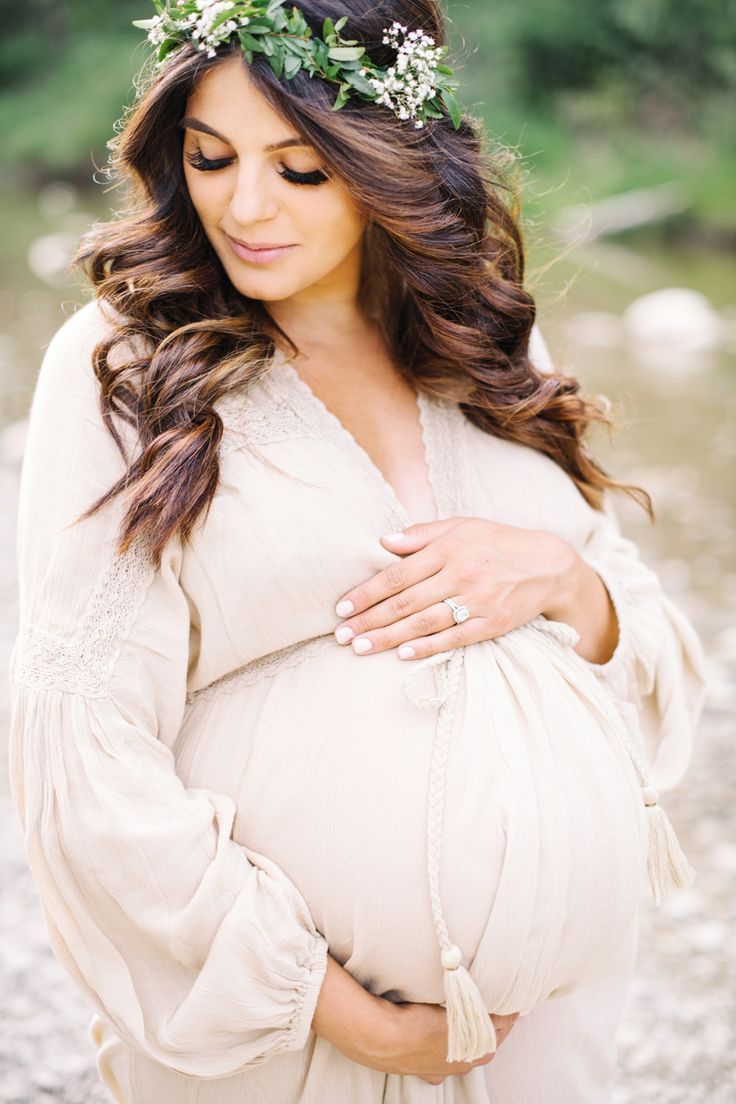 a pregnant woman wearing a flower crown and holding her belly in front of the camera