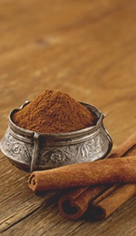 cinnamon sticks and powder in a silver bowl on a wooden table next to an orange peel