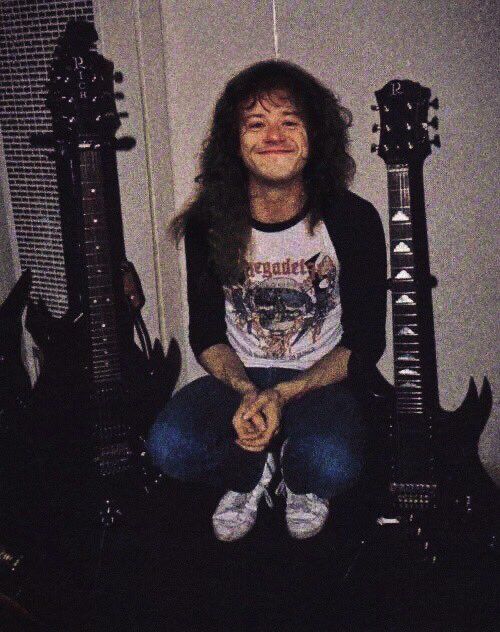 a man with long hair sitting in front of three electric guitars and smiling at the camera