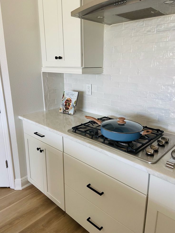 a stove top oven sitting inside of a kitchen next to white cupboards and drawers