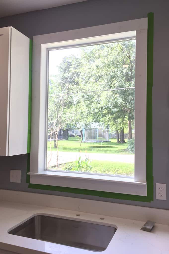 a kitchen window with green trim on the side and white cabinets in front of it