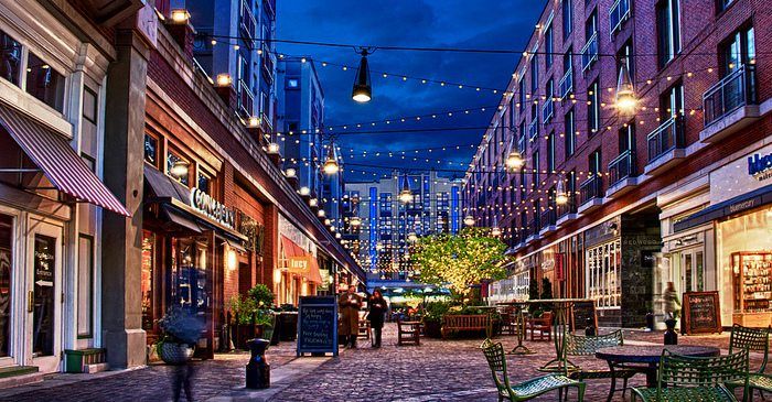 an empty city street with tables and chairs on the side walk at night, surrounded by tall buildings