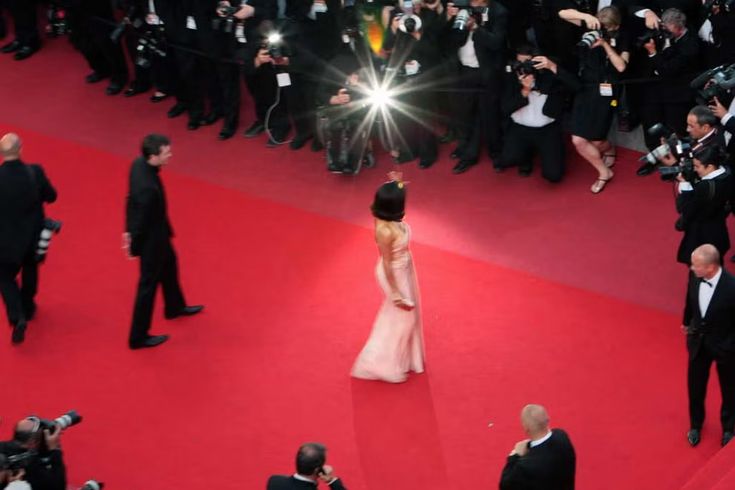 a woman in a pink dress is walking down the red carpet with cameras around her