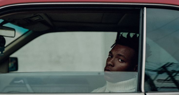 a man sitting in the passenger seat of a car looking out the window at something