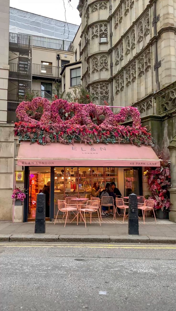 an outdoor cafe with pink flowers growing on the side of it's building and people sitting at tables outside