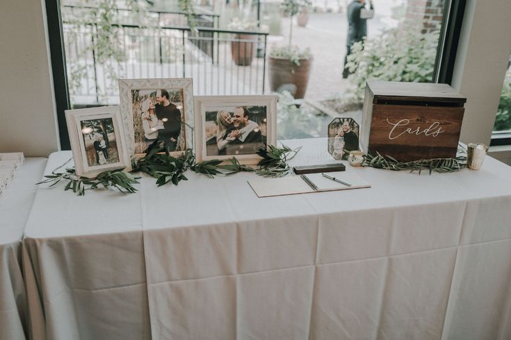 the table is set up with photos and greenery for an elegant wedding reception in front of a large window