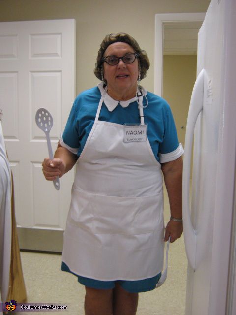 a woman wearing an apron and holding a spatula in her hand while standing next to a refrigerator